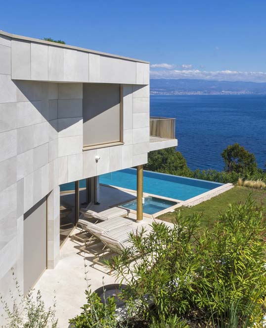 Façade contemporaine habillée de carrelage effet pierre claire intégrée au paysage côtier avec terrasse et piscine